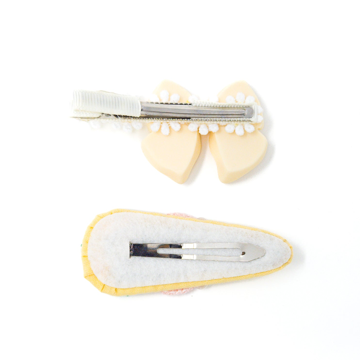 Two hair clips on white. One has a tan bow and white trim. The other has a yellow trim and white backing.
