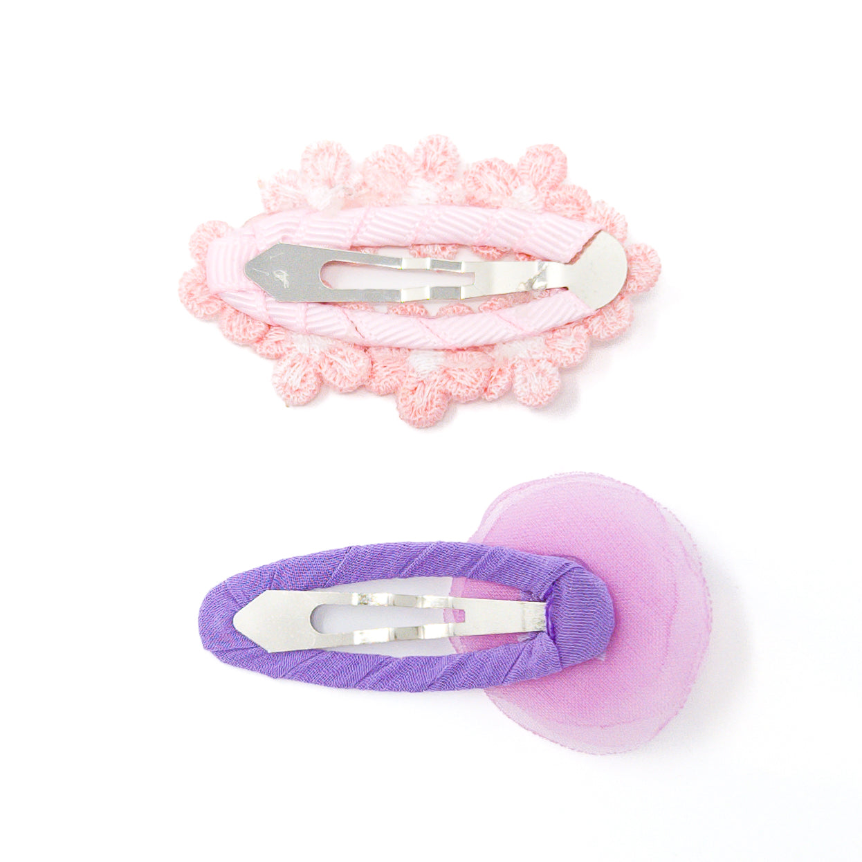Two hair clips on a white background. The top one is pink with a flower trim, and the bottom one is purple with a translucent pink fabric heart.