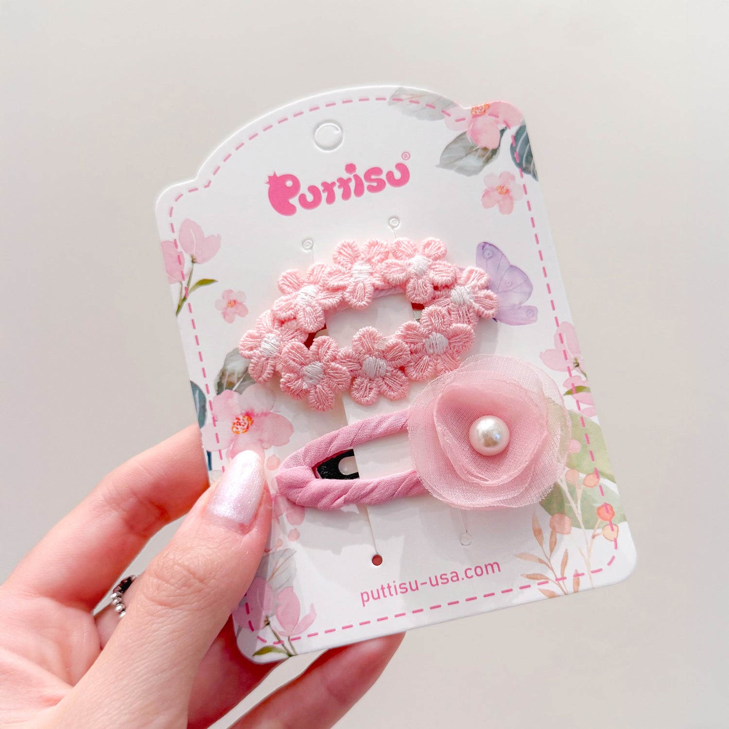 Close-up of two pink hair clips on a floral card being held by a hand.