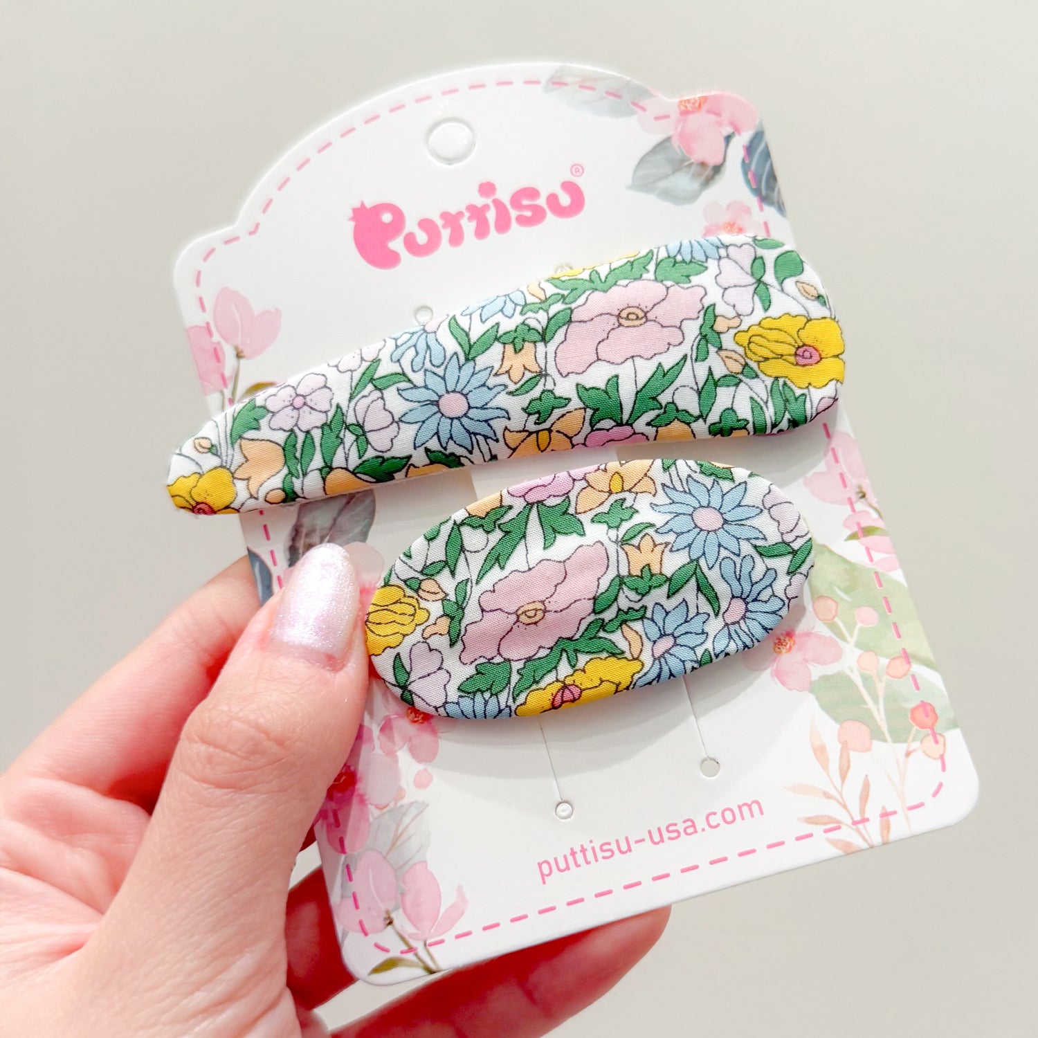 Two floral hair clips on a card being held in a hand.