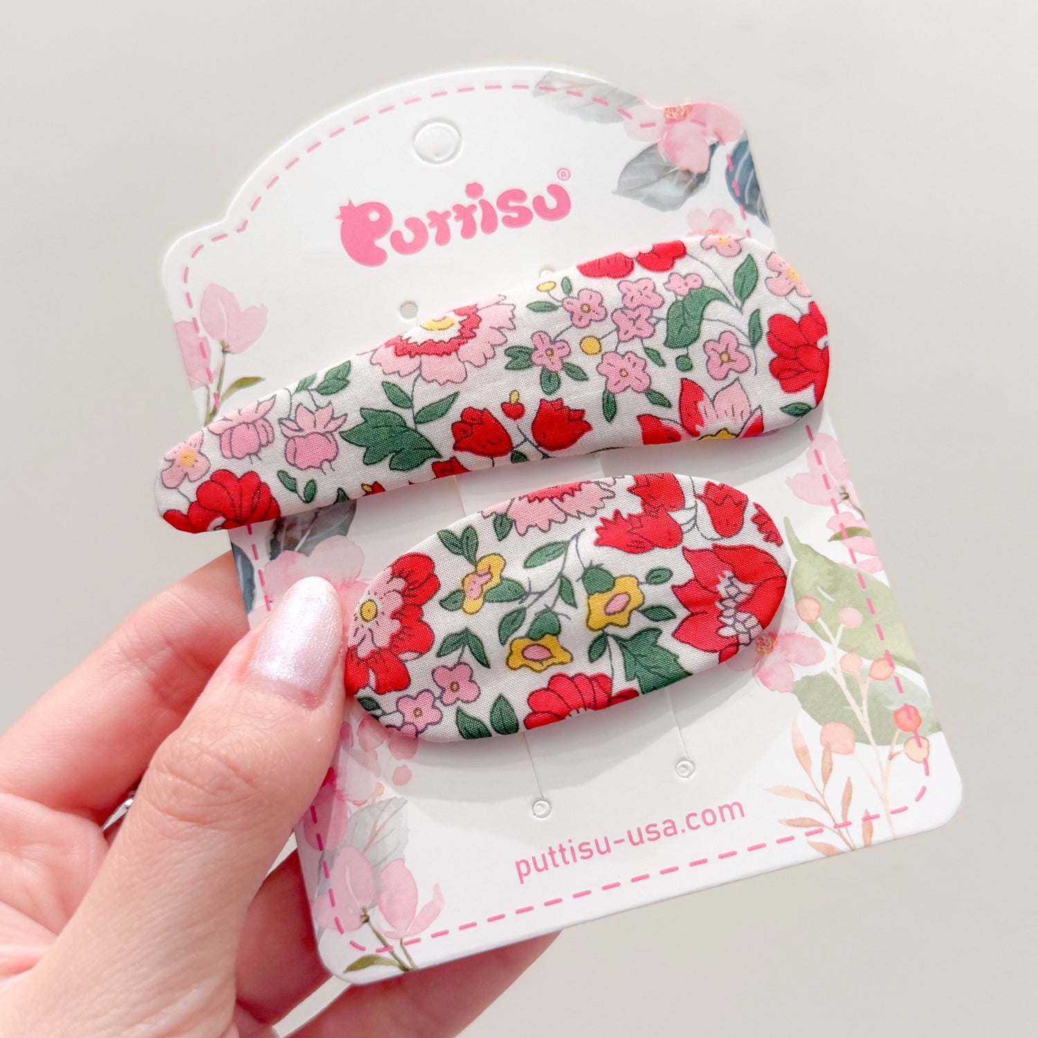 Two floral print hair clips on a decorative card held in a hand.