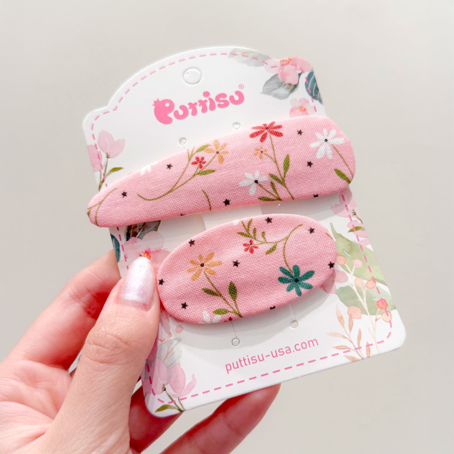 Two pink floral fabric hair clips on a patterned card.