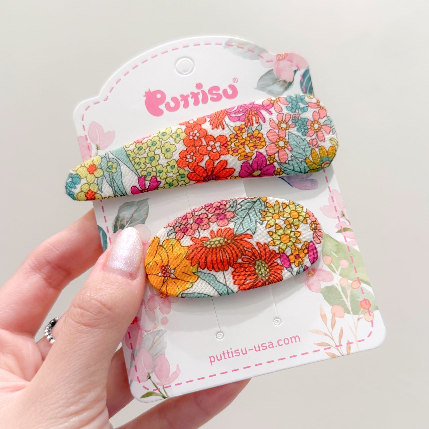 Two floral hair clips on a display card being held by a hand.