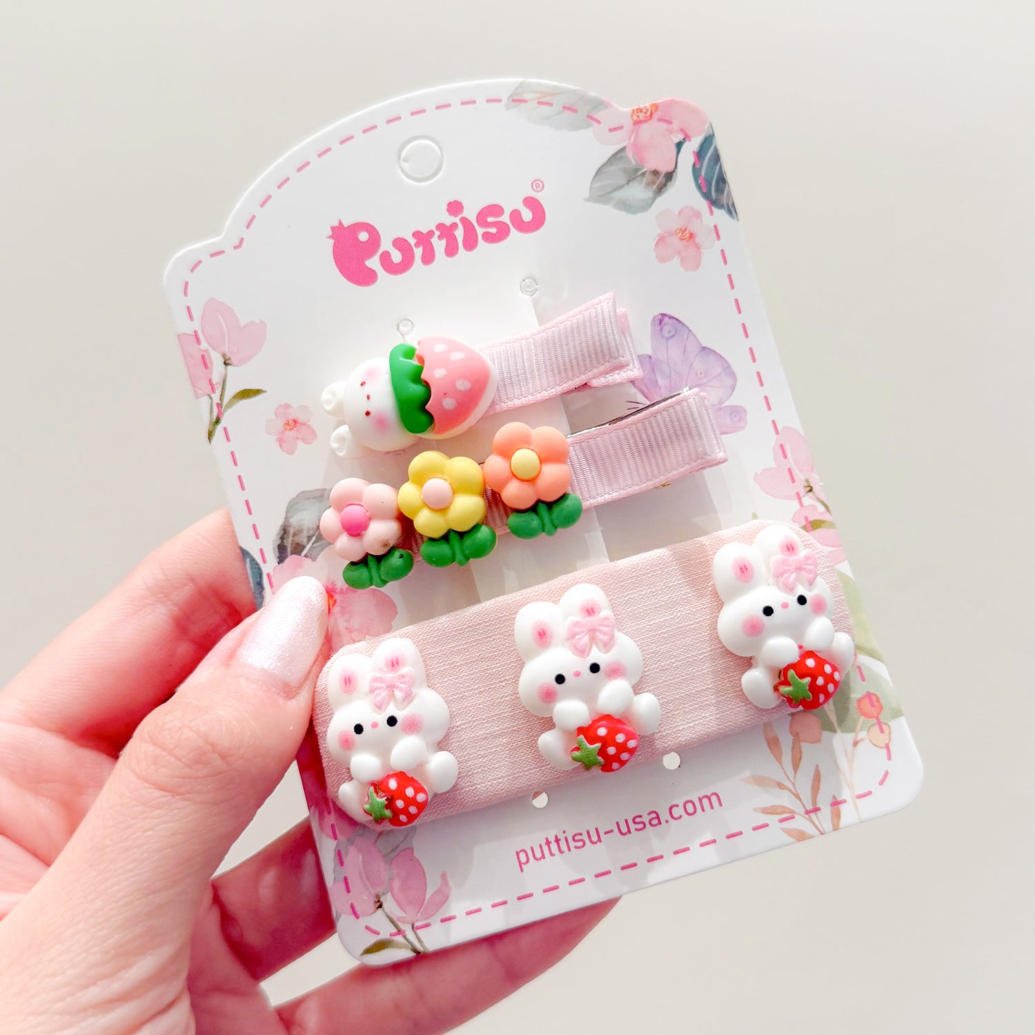 Three hair clips with pink ribbons, flowers, and rabbits on a pink and white floral backing.