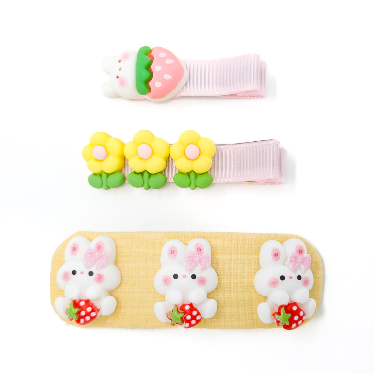 Three children's accessories: a strawberry-shaped clip, a floral clip, and a bandage with bunny designs.