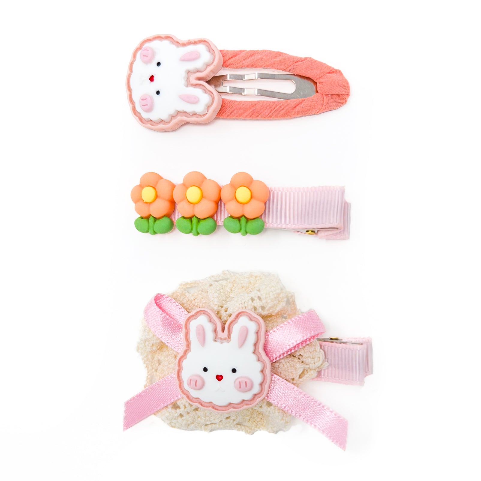 Three hair clips on a white background. One is a pink bunny clip with a pink fabric-covered clip. The second has orange flowers on a pink ribbon-covered clip. The third is a pink bow tied over a lace clip with a white bunny.