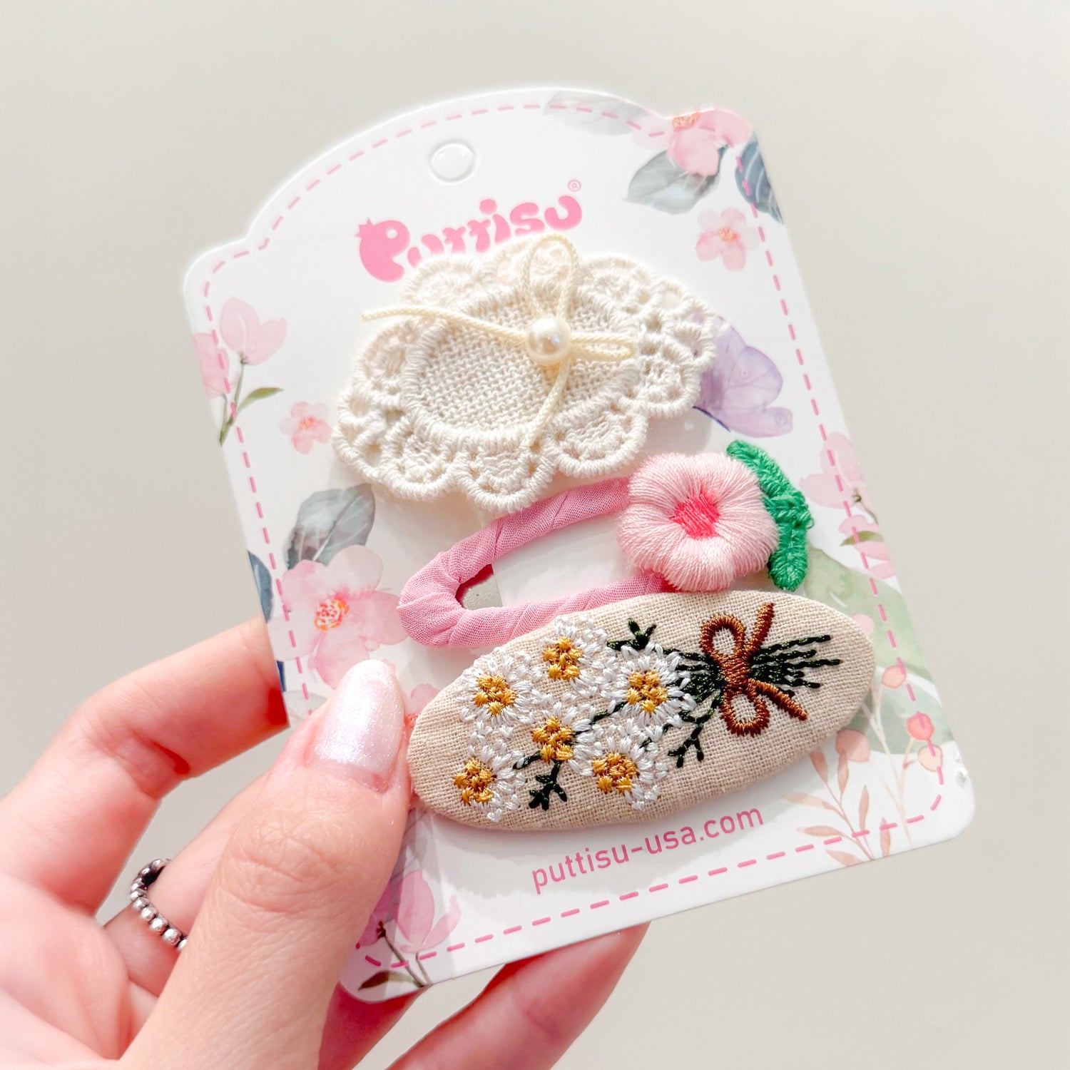 Close-up of hand holding a product card of three embroidered hair clips.