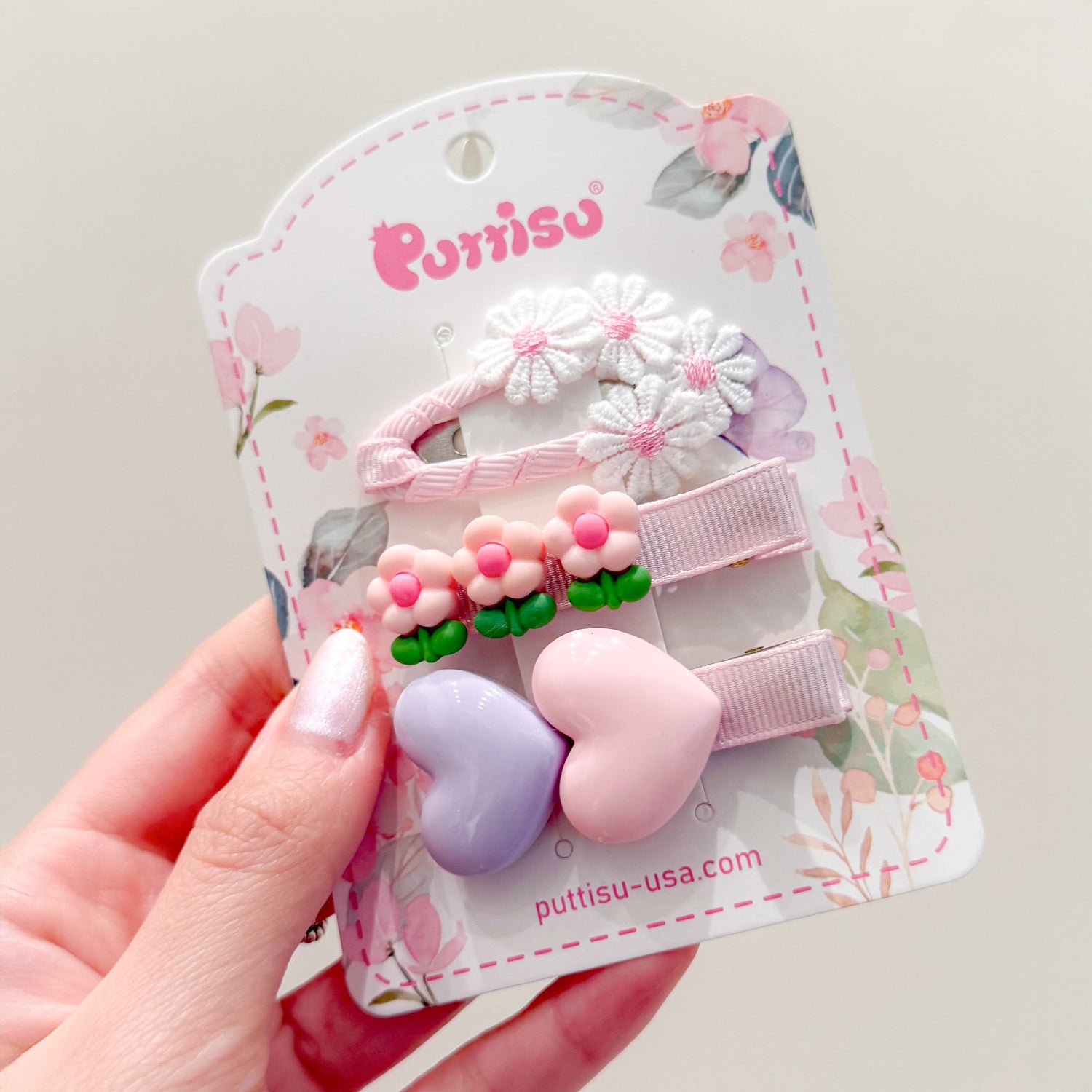 A hand holding a card of children's hair clips with flower and heart designs.