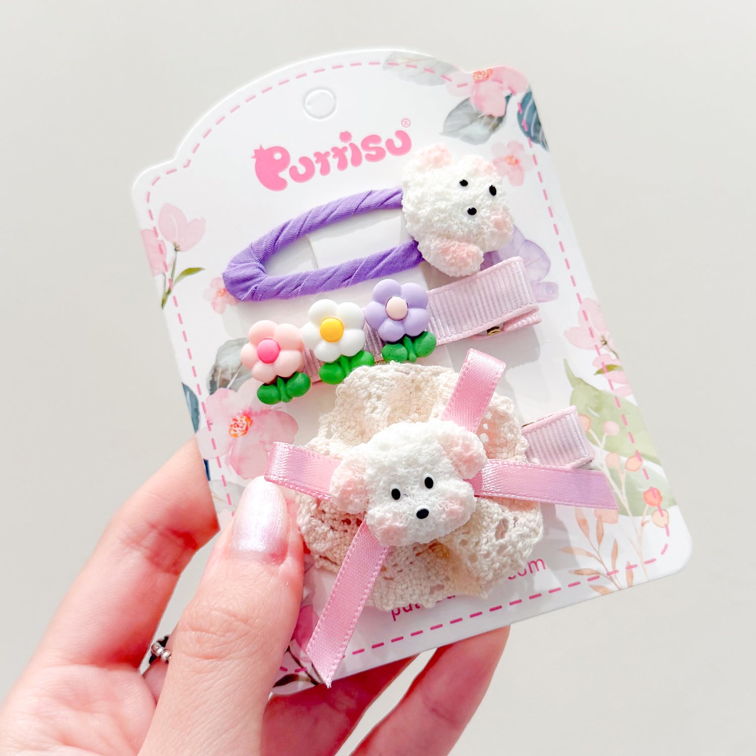 Hair clips on a floral-patterned card. The clips feature teddy bear, flower, and ribbon designs.