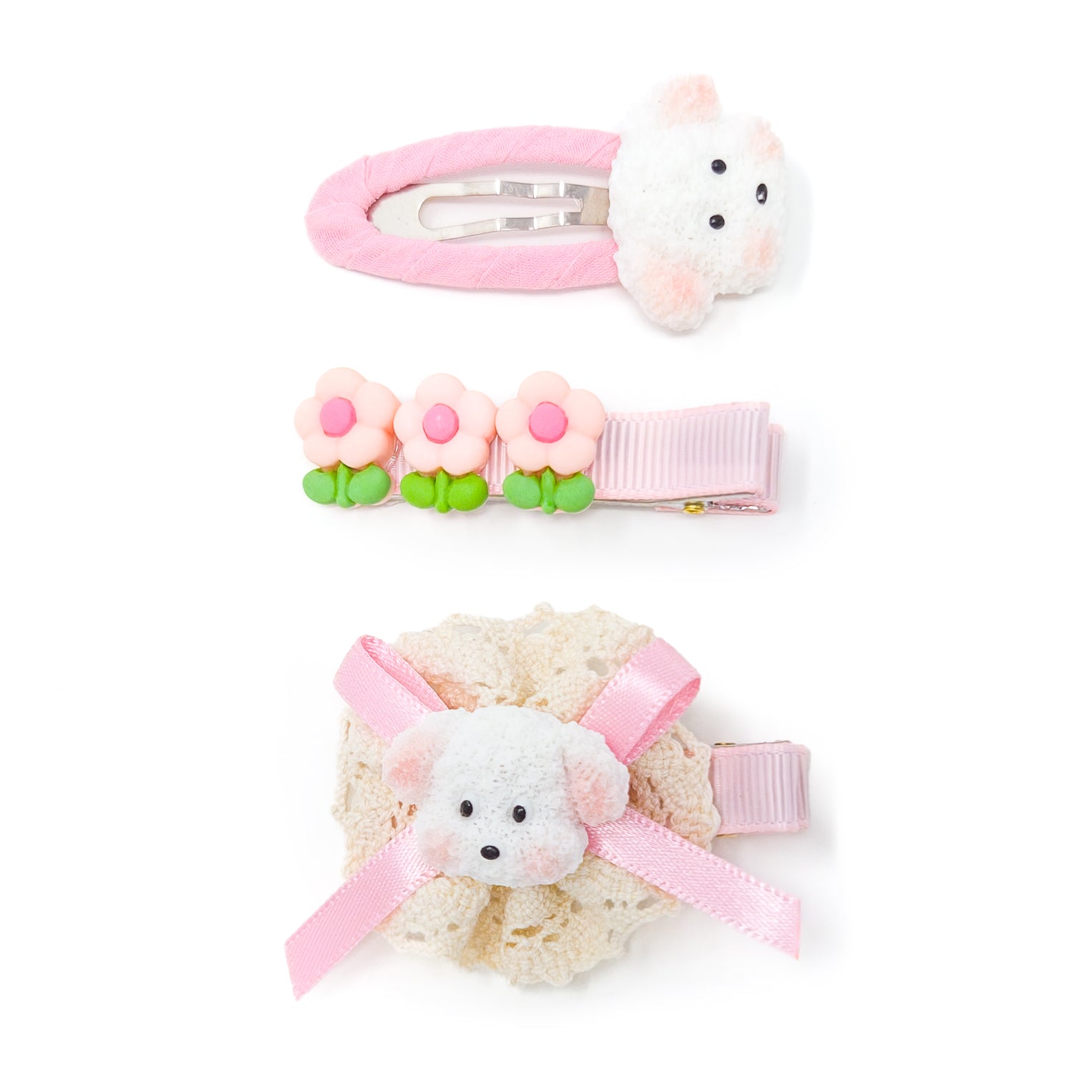 Three girls' hair clips. The top clip features a pink fabric covering and a white bunny head. The middle clip has three small pink flowers and a pink ribbon. The bottom clip includes a white dog's head, a pink ribbon, and a cream-colored crochet detail.