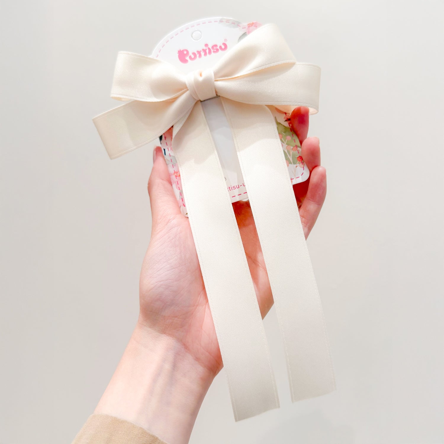 Hand holding a floral print package with a large cream-colored ribbon bow.