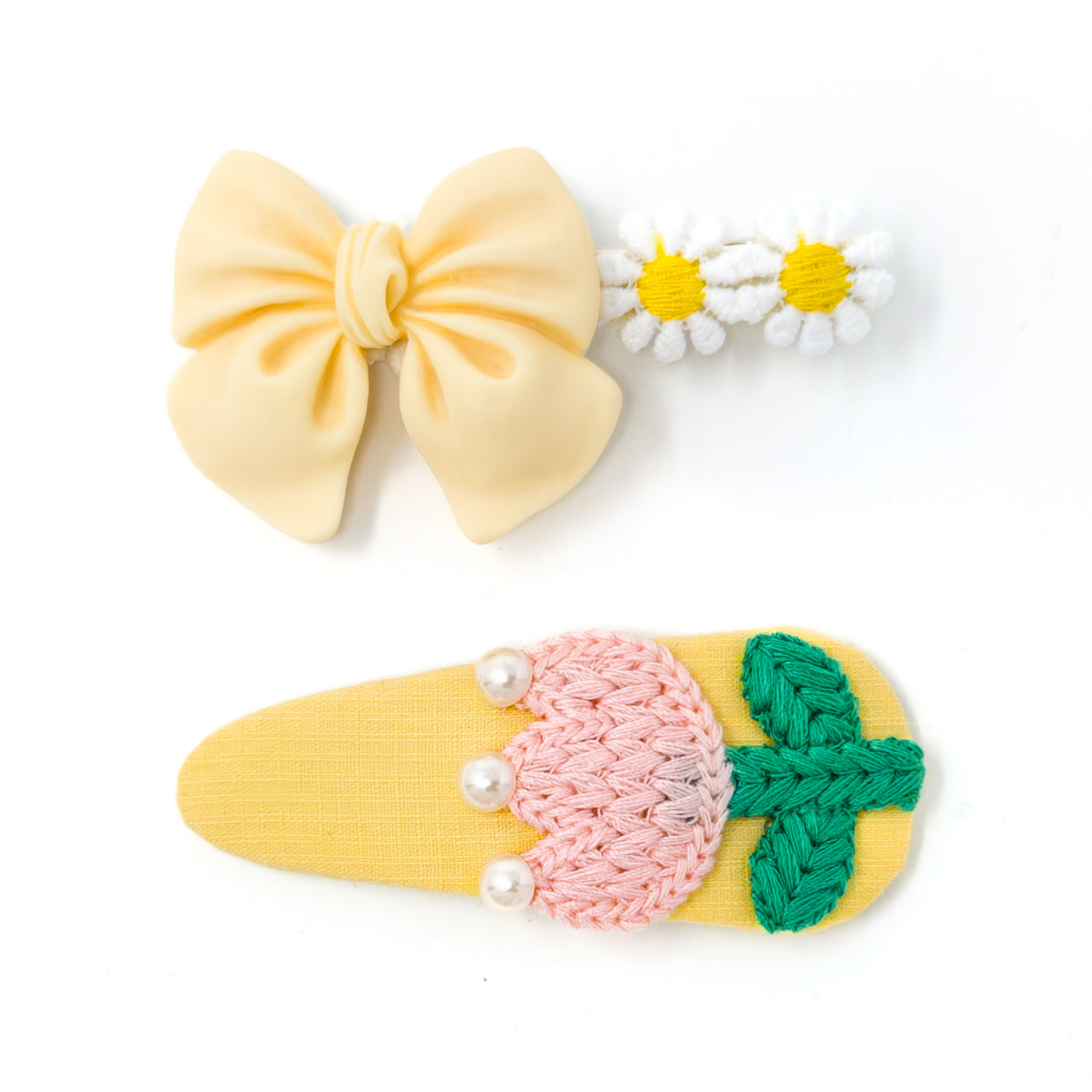 Three hair clips: a yellow bow, two daisies, and a yellow clip with pink knitting, green embroidery, and three white pearls.