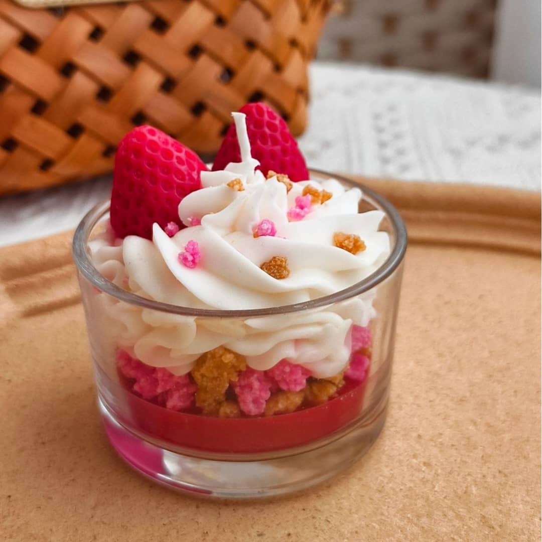 Small dessert in a glass with whipped cream, strawberries, and colorful toppings on a wooden surface.