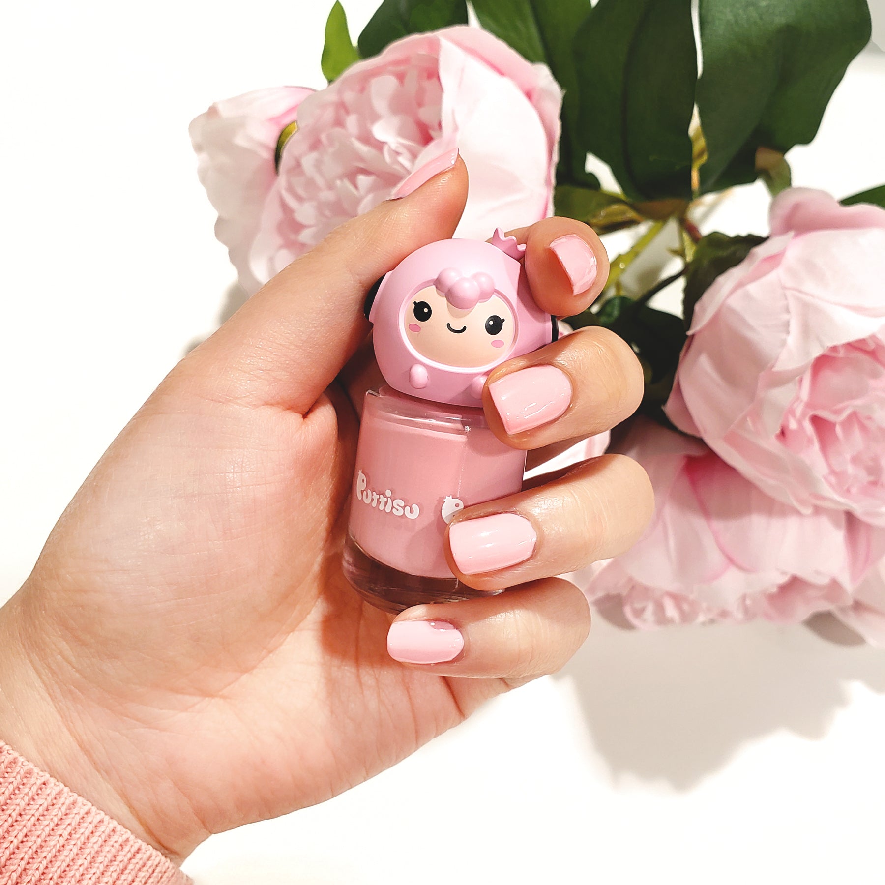 Hand holding a pink bottle of Pororo nail polish with pink flowers in the background.