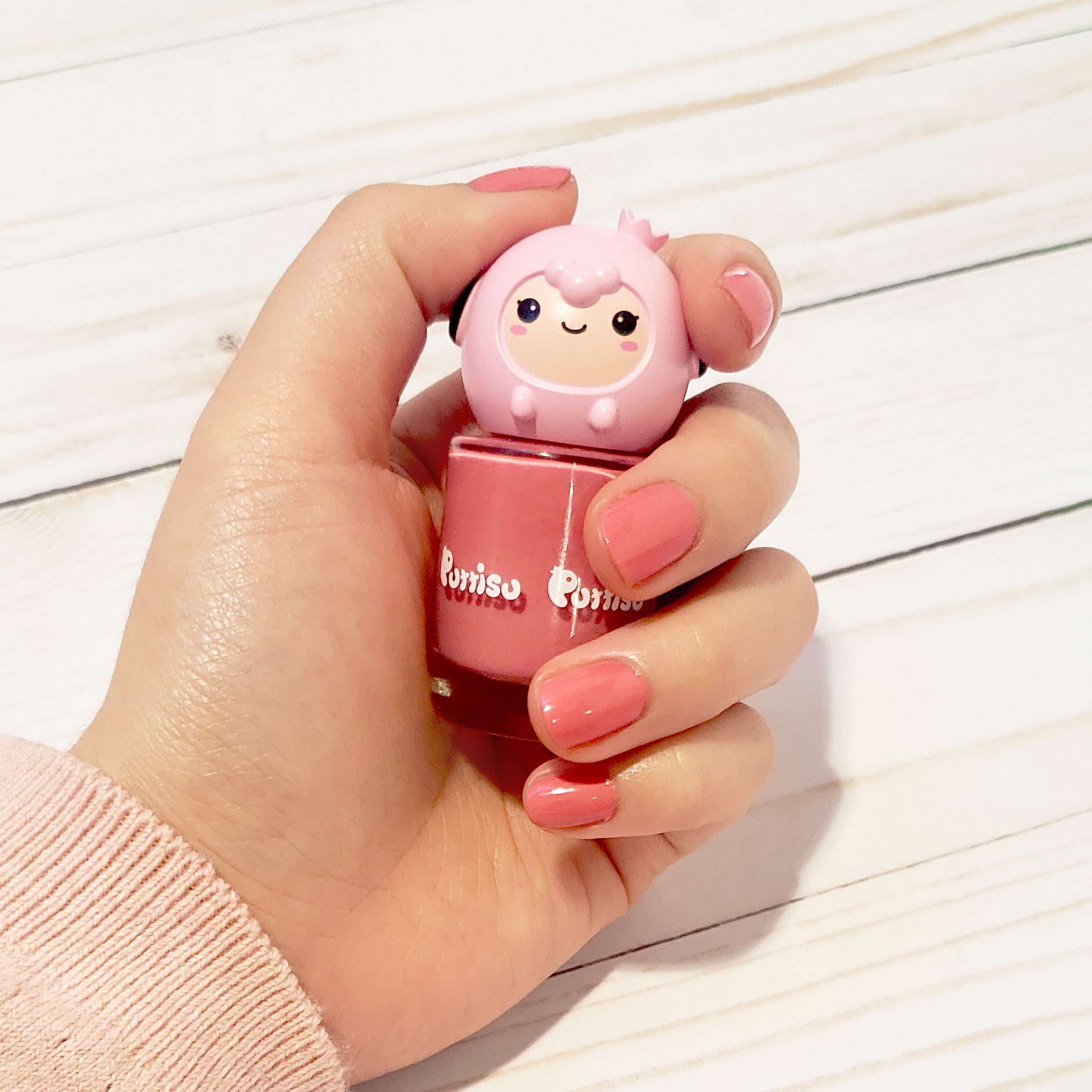 Hand holding pink Pororo nail polish bottle on a white wood surface.