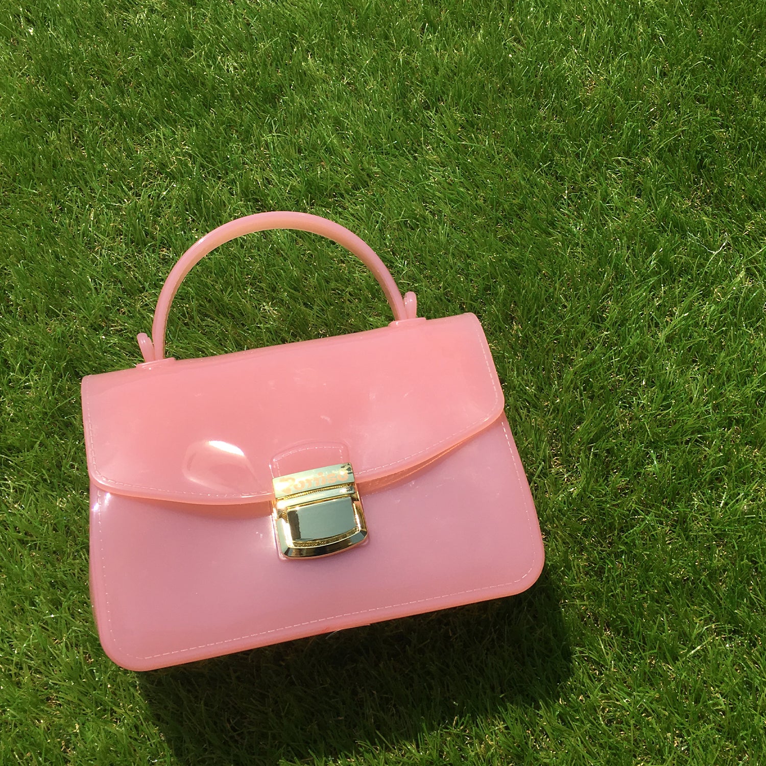 Pink plastic purse with gold clasp on grass.