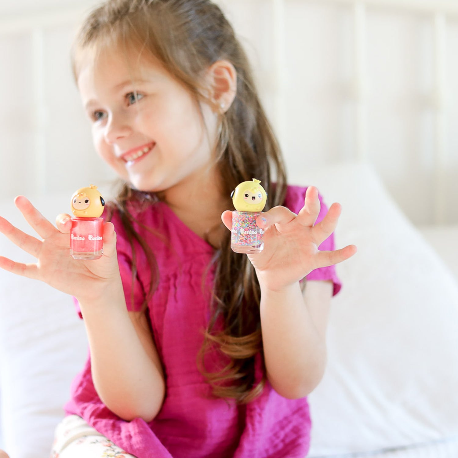A smiling girl in a pink shirt holds two bottles of colorful nail polish.