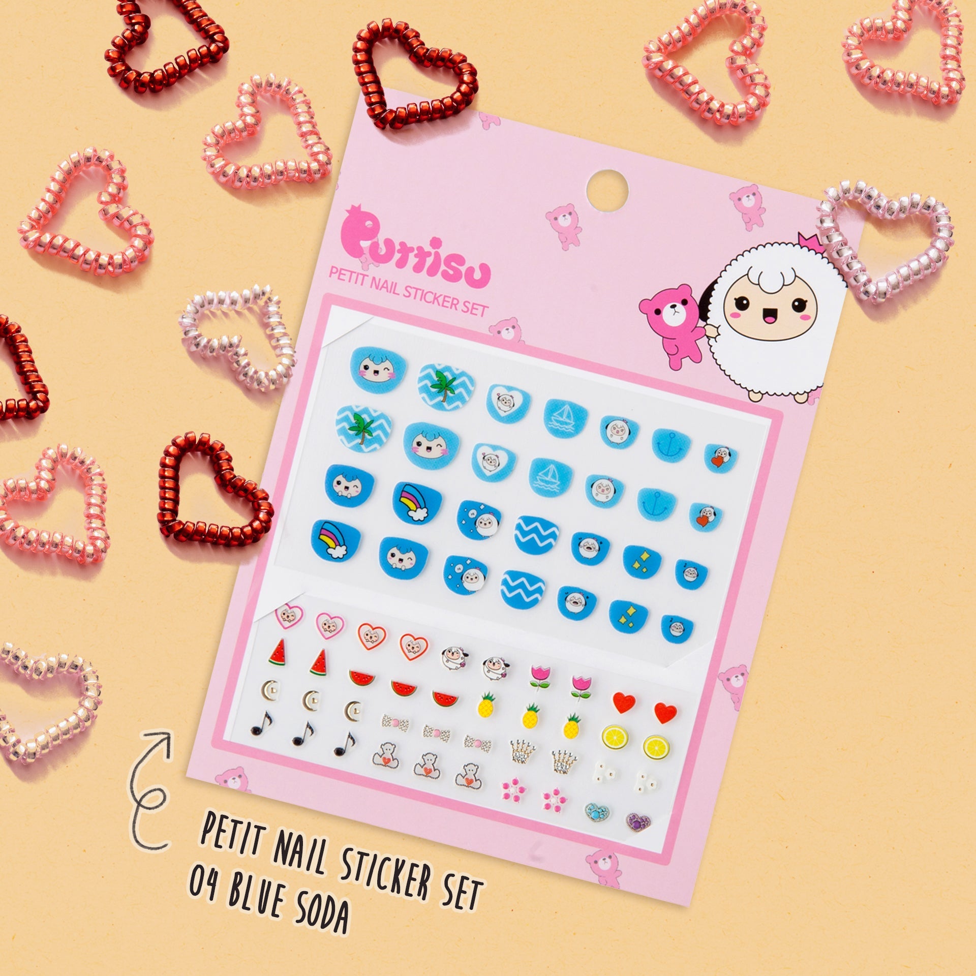 A pink sheet of Purrisu Petit Nail Stickers with blue and pastel stickers, surrounded by heart-shaped metal hair ties.