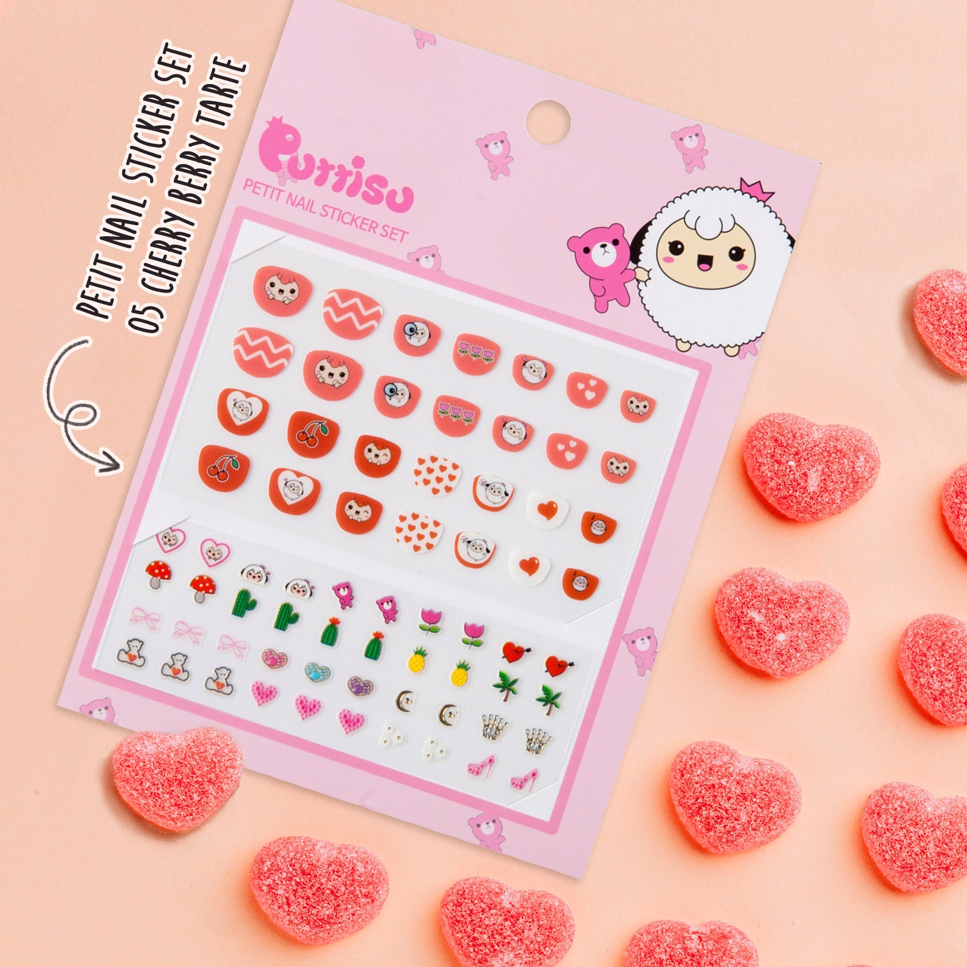 A pink package of "Purriso" nail stickers titled "Petit Nail Sticker Set 05 Cherry Berry Tarte," resting on a light peach background and surrounded by heart-shaped candies.