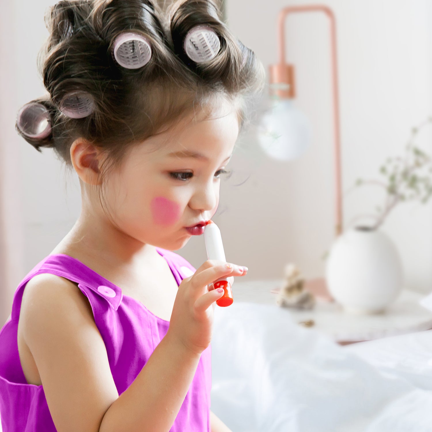 Young girl in curlers and a purple dress applies red lipstick.