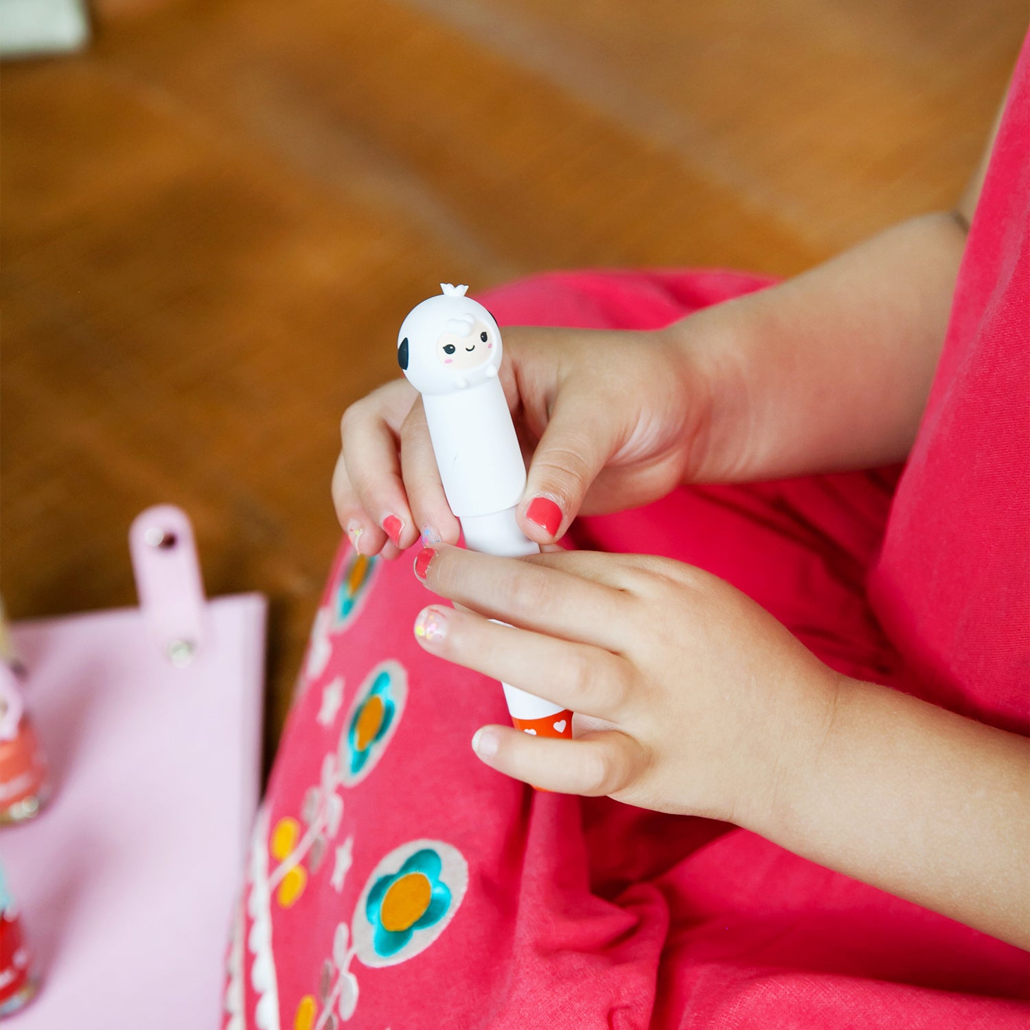 Child holding a white pen with a cartoon face on a red printed dress.
