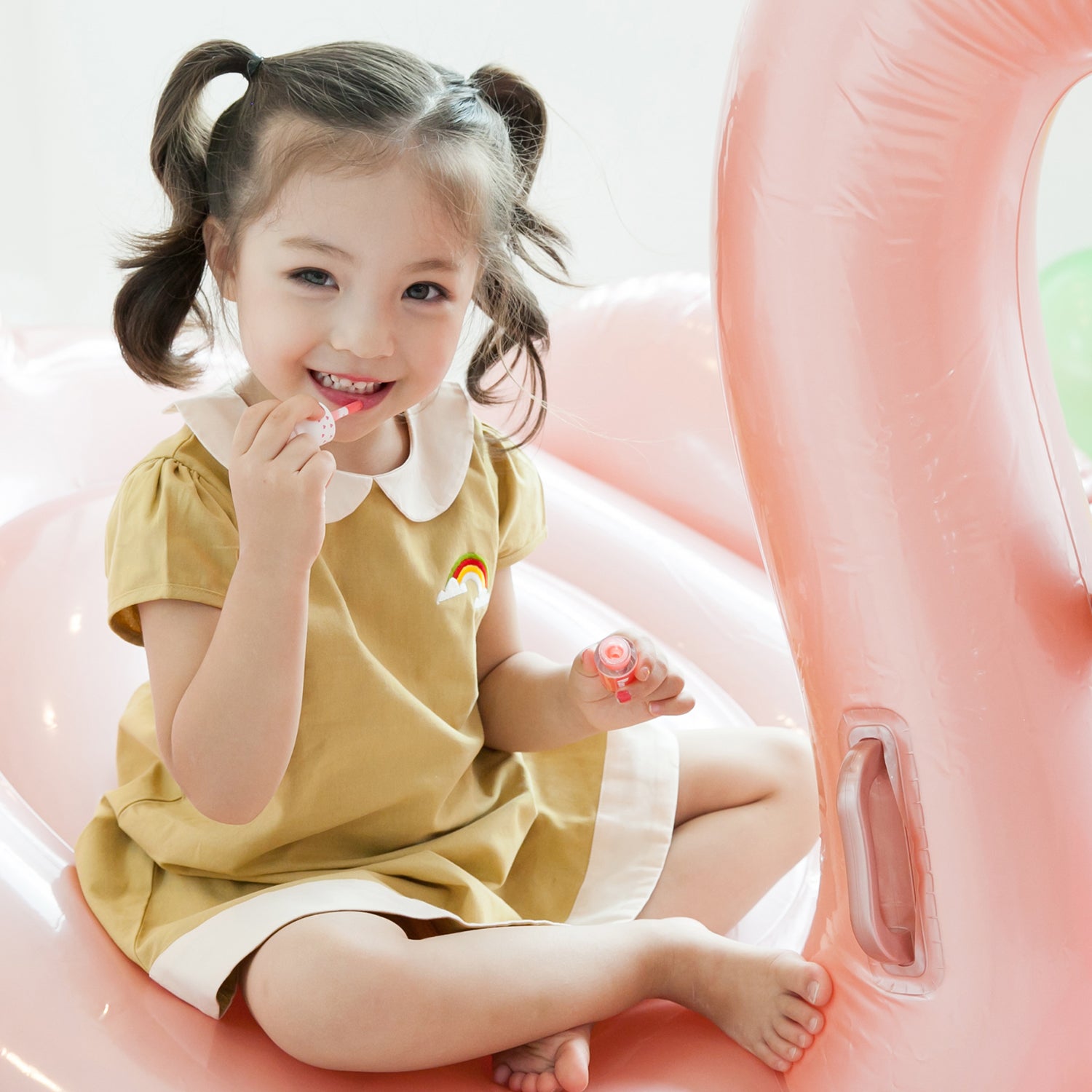 Child sitting on a pink inflatable, wearing a mustard-yellow dress.