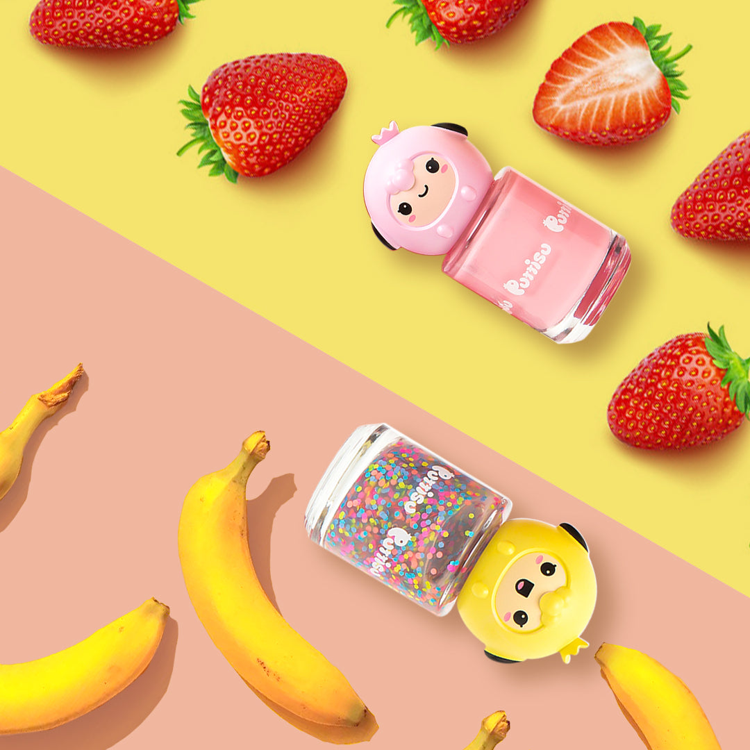 Overhead shot of pink nail polish with a sheep head and iridescent glitter polish with a chick head, with strawberries on a yellow background and bananas on a pink background.