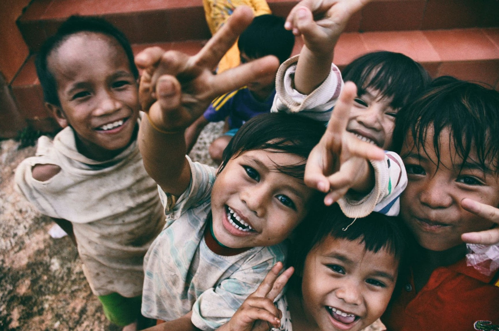 Happy children laughing and showing peace signs while playing together outdoors.