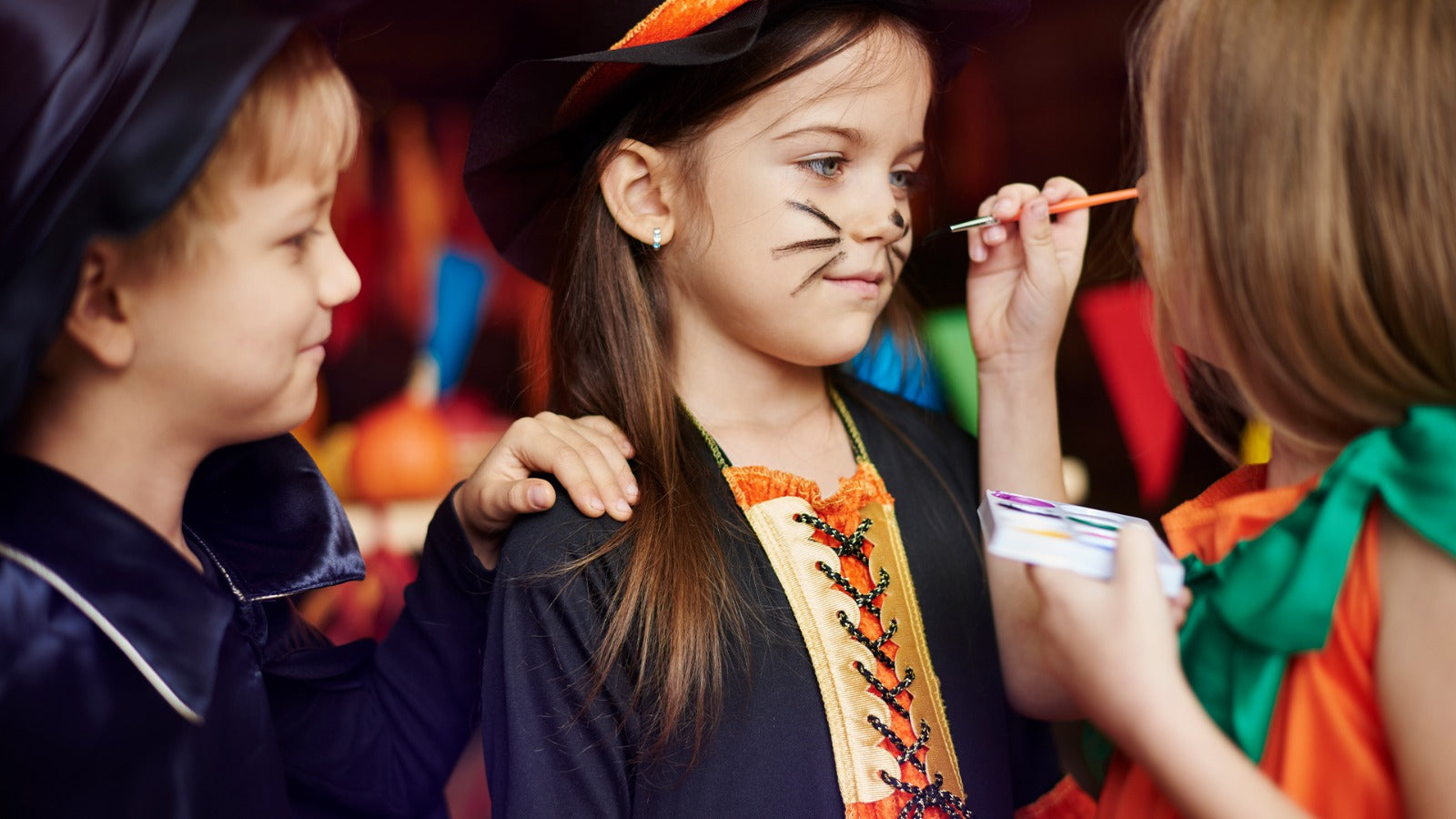 Children in Halloween costumes enjoying face painting activity during a festive party.