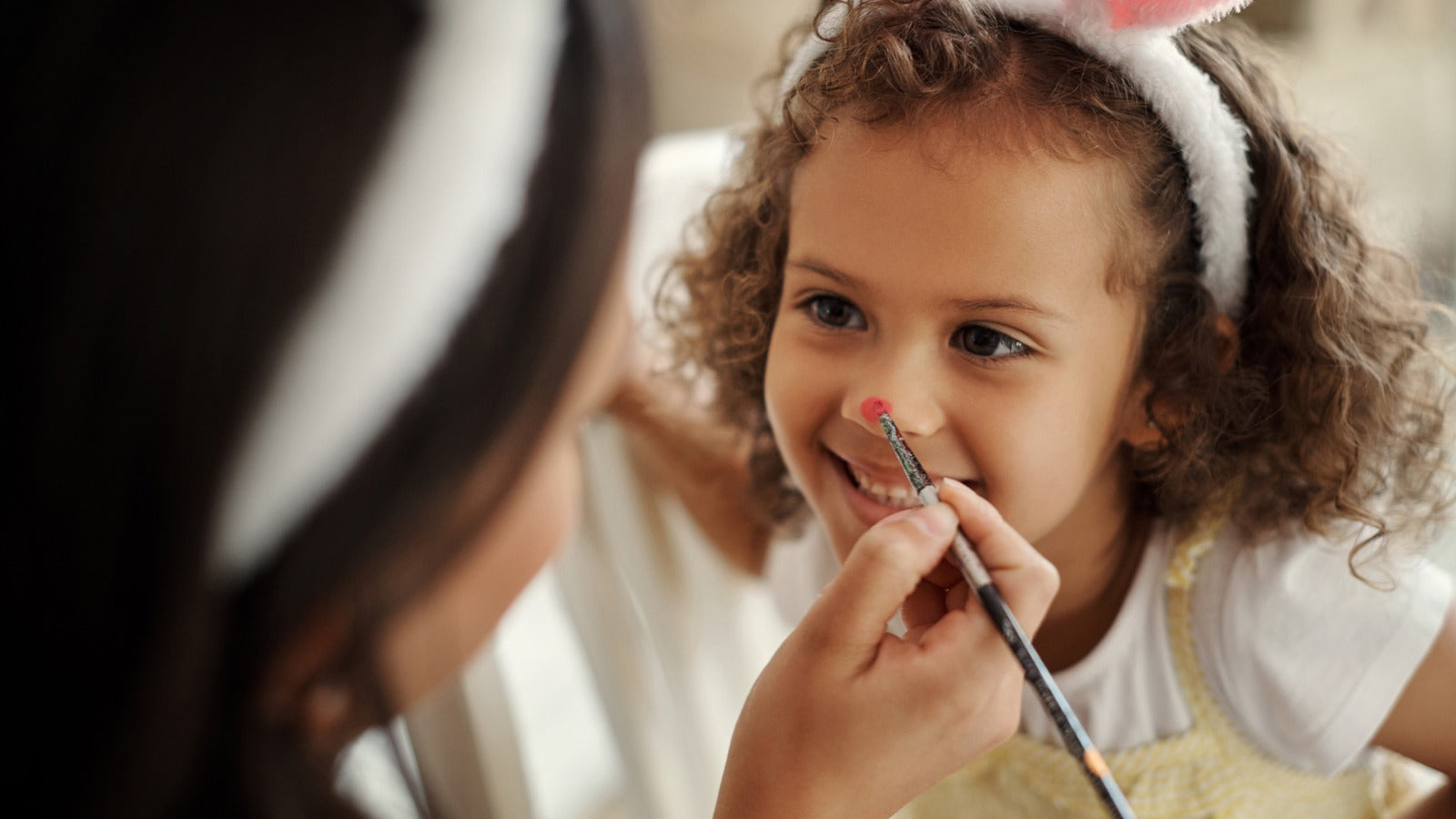 Child in bunny ears enjoying face painting activity at a fun event.