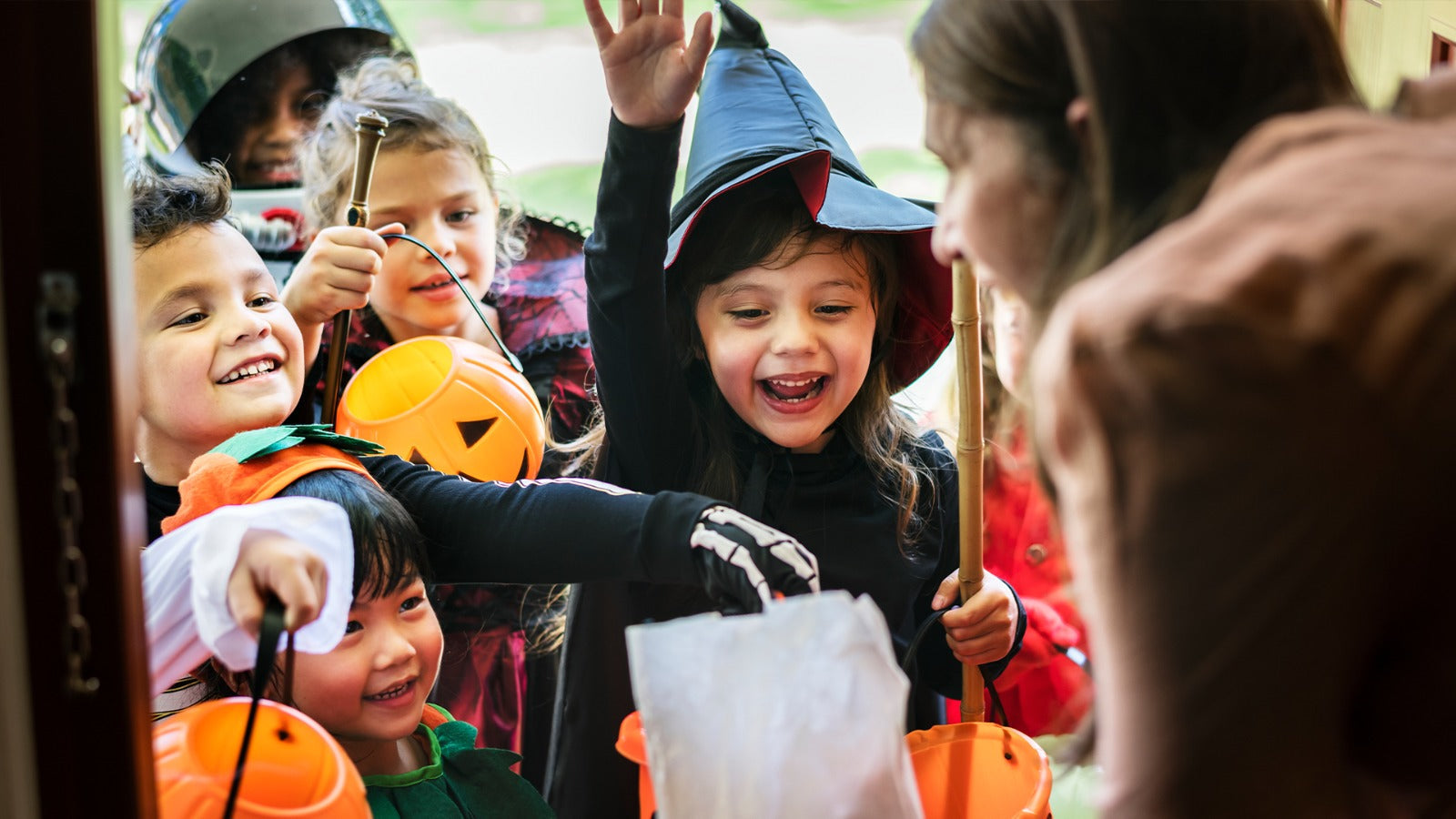 Excited kids in Halloween costumes trick-or-treating with pumpkin candy buckets.