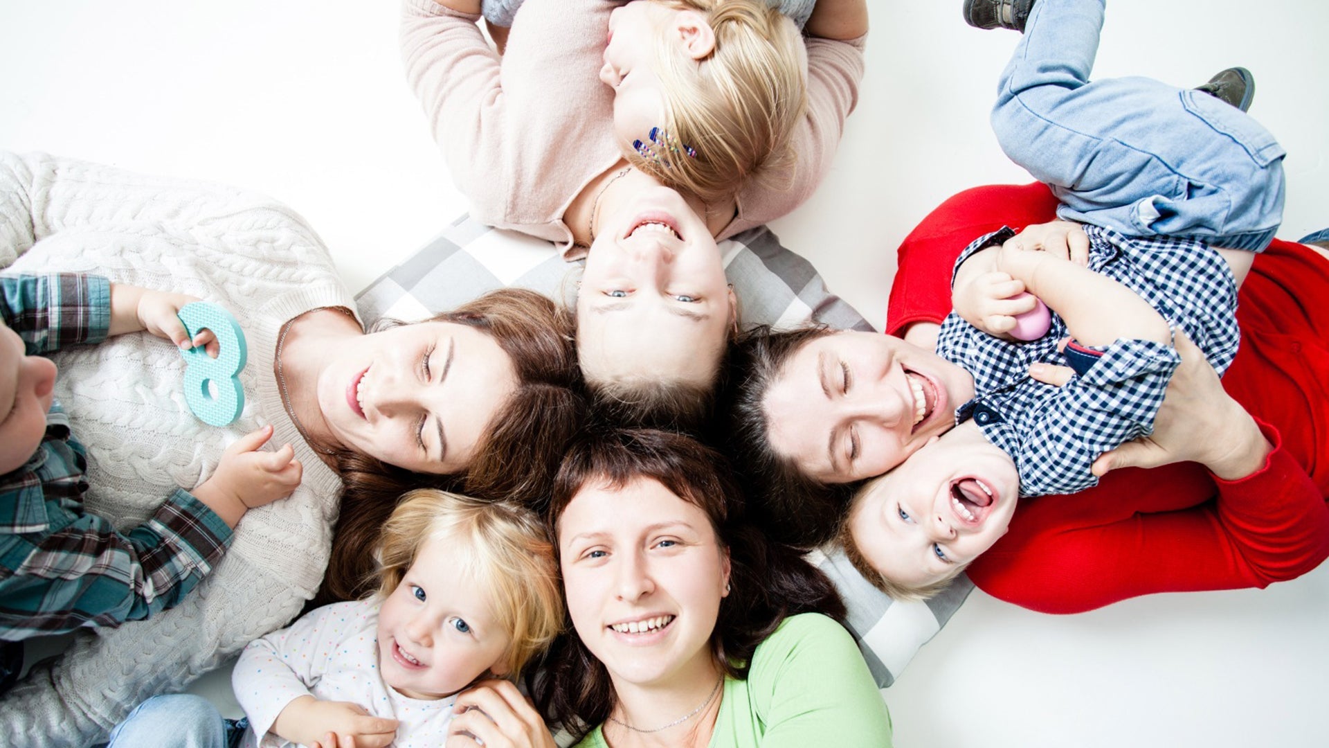 Happy mothers and children lying together in a circle, smiling and playing indoors.