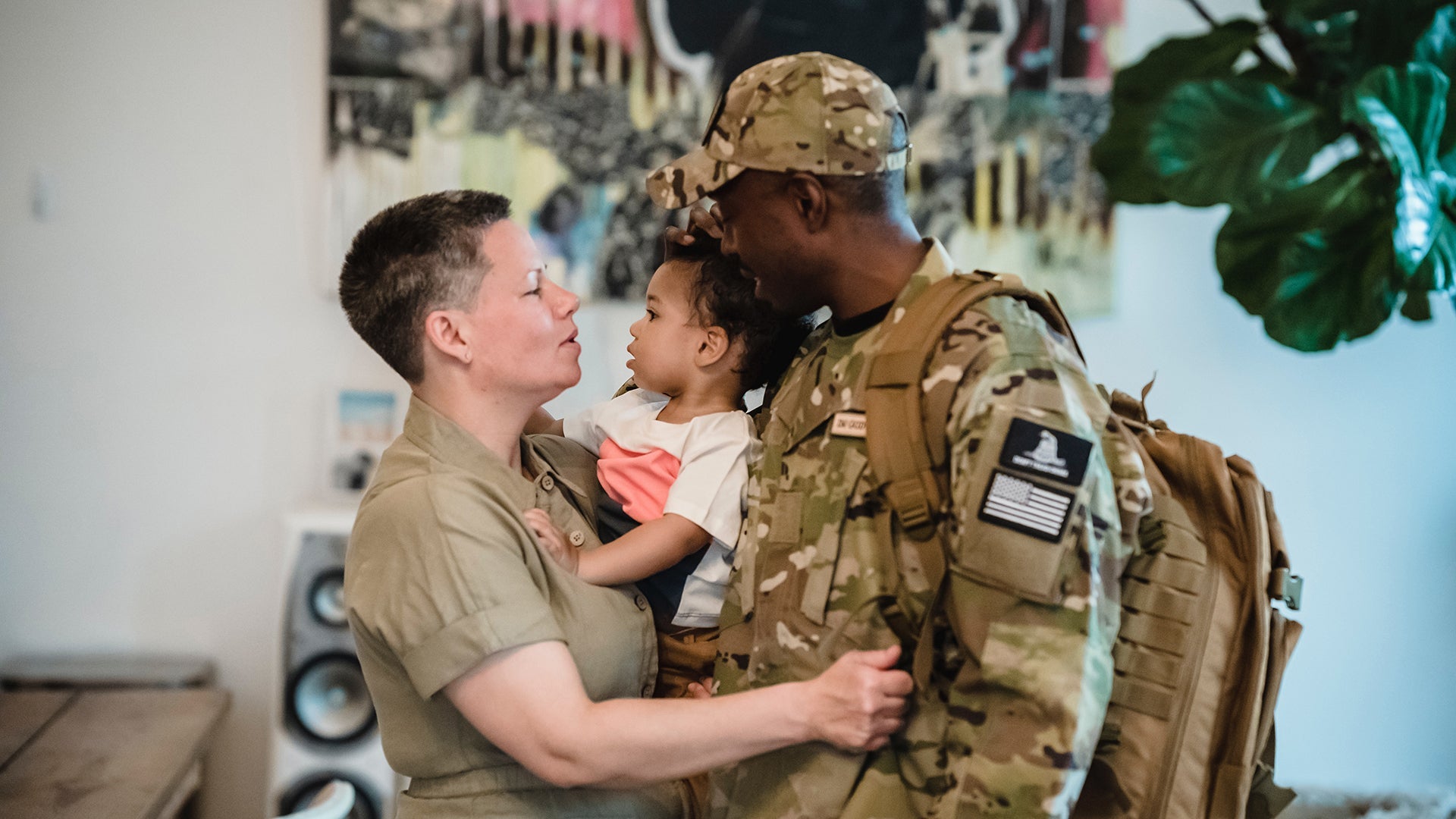 Military family reunion with soldier in uniform embracing partner and child at home