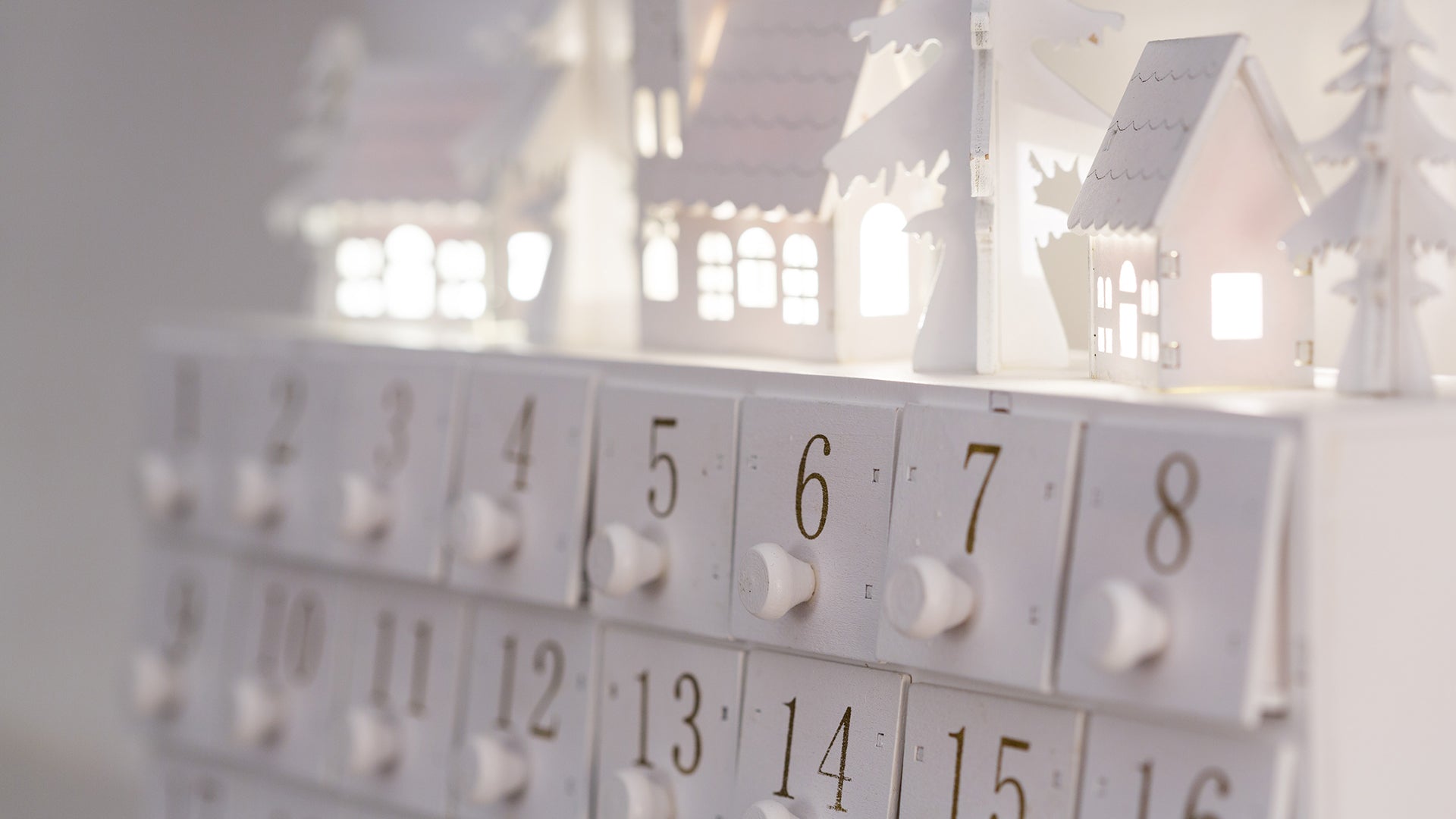 White wooden advent calendar with numbered drawers and festive holiday village decorations.