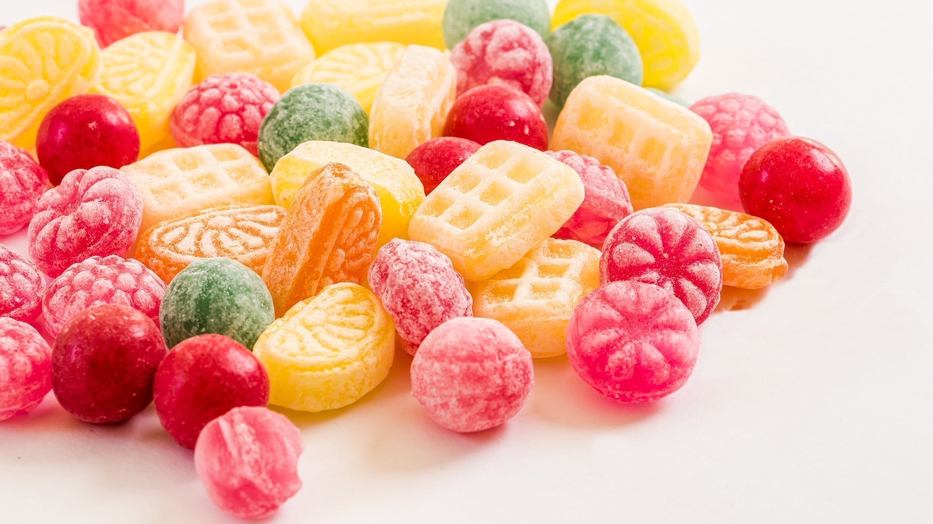 Bright assortment of colorful hard candies in red, yellow, green, and orange on white background.
