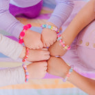 Close-up of five children's hands touching fists, each wearing a colorful beaded bracelet.