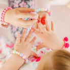 Two girls applying nail polish; one wears a pink pompom bracelet.