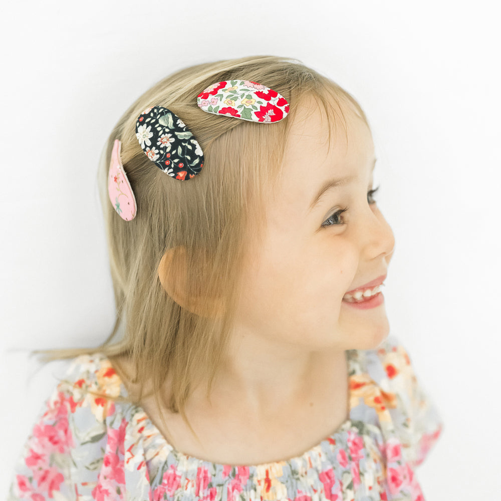 Child with colorful oval-shaped floral-pattern hair clips on a white background