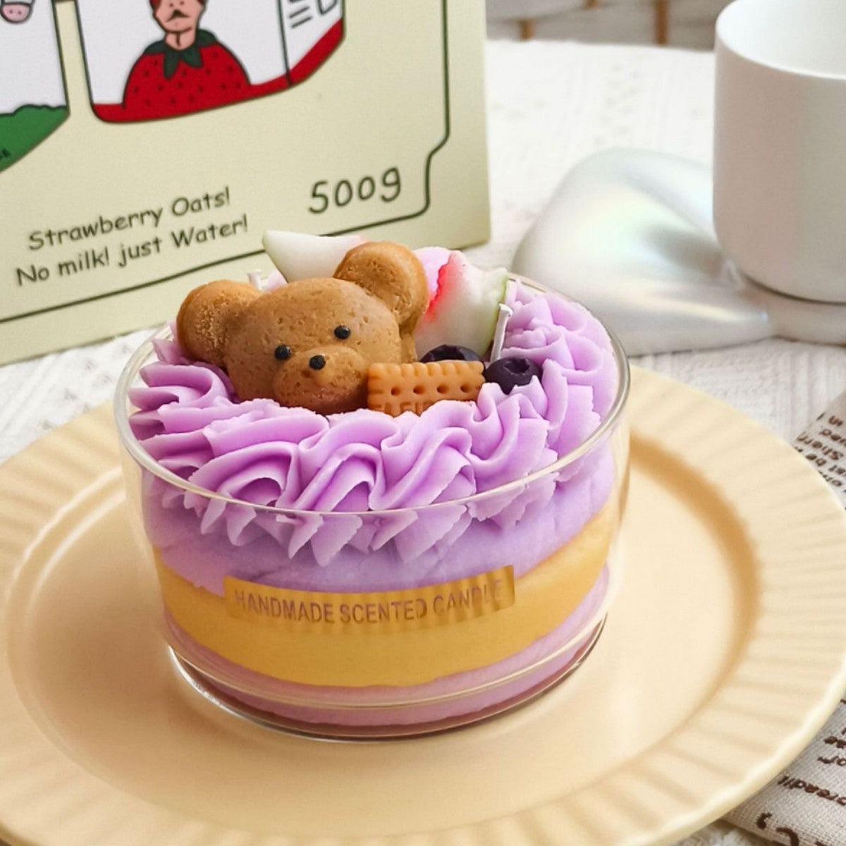 Jellycup cake soy wax candle with purple frosting, decorated with a teddy bear and fruit.
