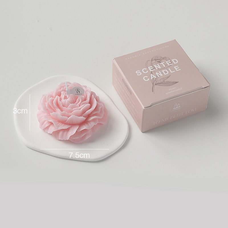 Pink soy wax candle in the shape of a flower by Jellycup, sitting on a white dish next to its box.
