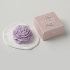 Lavender peonie flower soy wax candle by Jellycup, on a white plate, next to its box.