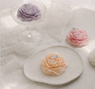 Peony flower soy wax candles in various colors, displayed with a lacy cloth and arranged attractively.
