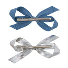 Two bow clips, one light denim and one silver, shown from the back with their metal clips.