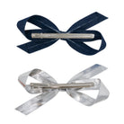 Two bow clips, one light denim and one silver metallic, each with a silver alligator clip on the back.