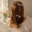 Pink ribbon bow clip set styled in long brown hair with a braided section, viewed from the back.