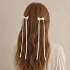 Ivory Ribbon Bow Clip Set, two clips with long trailing ribbons securing sections of wavy brown hair from behind.