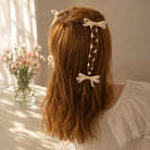 Four ivory ribbon bow clips styling long reddish-brown hair, with one braided into a single strand, worn with a white ruffled blouse.