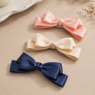 Blush and ivory large satin double bow clip set, arranged with a navy clip on a beige surface.