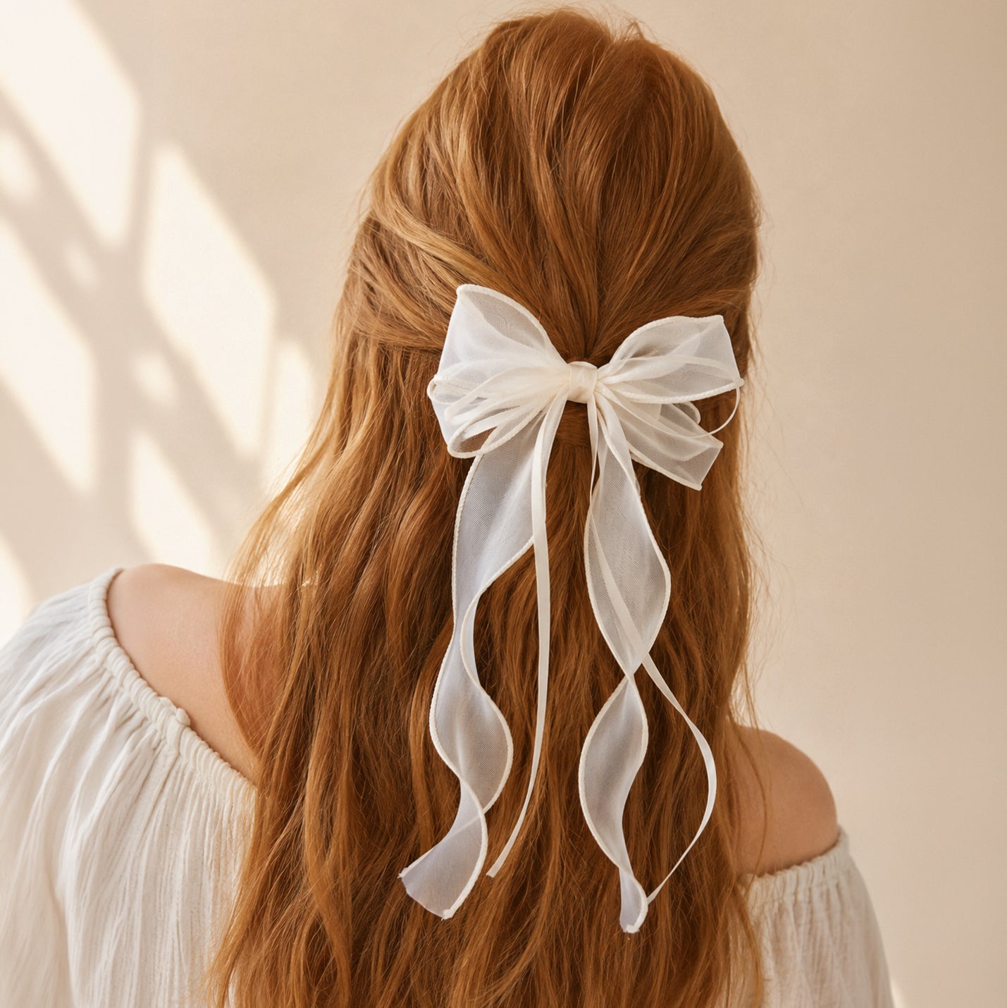 White organza double ribbon clip in reddish-brown hair styled half-up, with long flowing ribbons, worn with a white off-shoulder top.