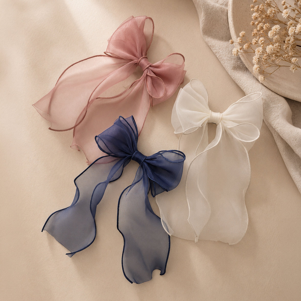 Three organza large bow clips in pink, navy, and white, each with long, wavy, sheer ribbon tails on a light surface.